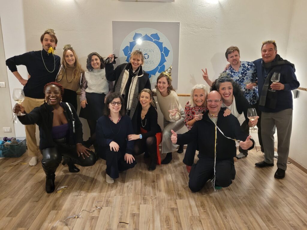 Joyful mixed-age group toasting with wine, posing together on wooden floor