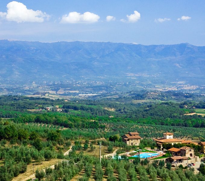 Expansive valley of olive groves and farmhouses beneath distant blue mountains